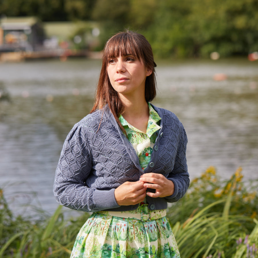 woman wearing a pastel blue knitted summer cardigan and a green striped shirt dress