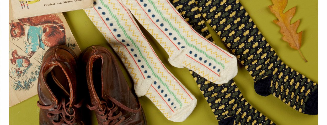 Flat lay image of childrens tights, cream with red pinstripes ,blue dots, green pinstripes and mustard squiggles. Also Navy tights with yellow and green flecks. Carefully arranged on a lime green surface with old children's books and an oak leaf or two.