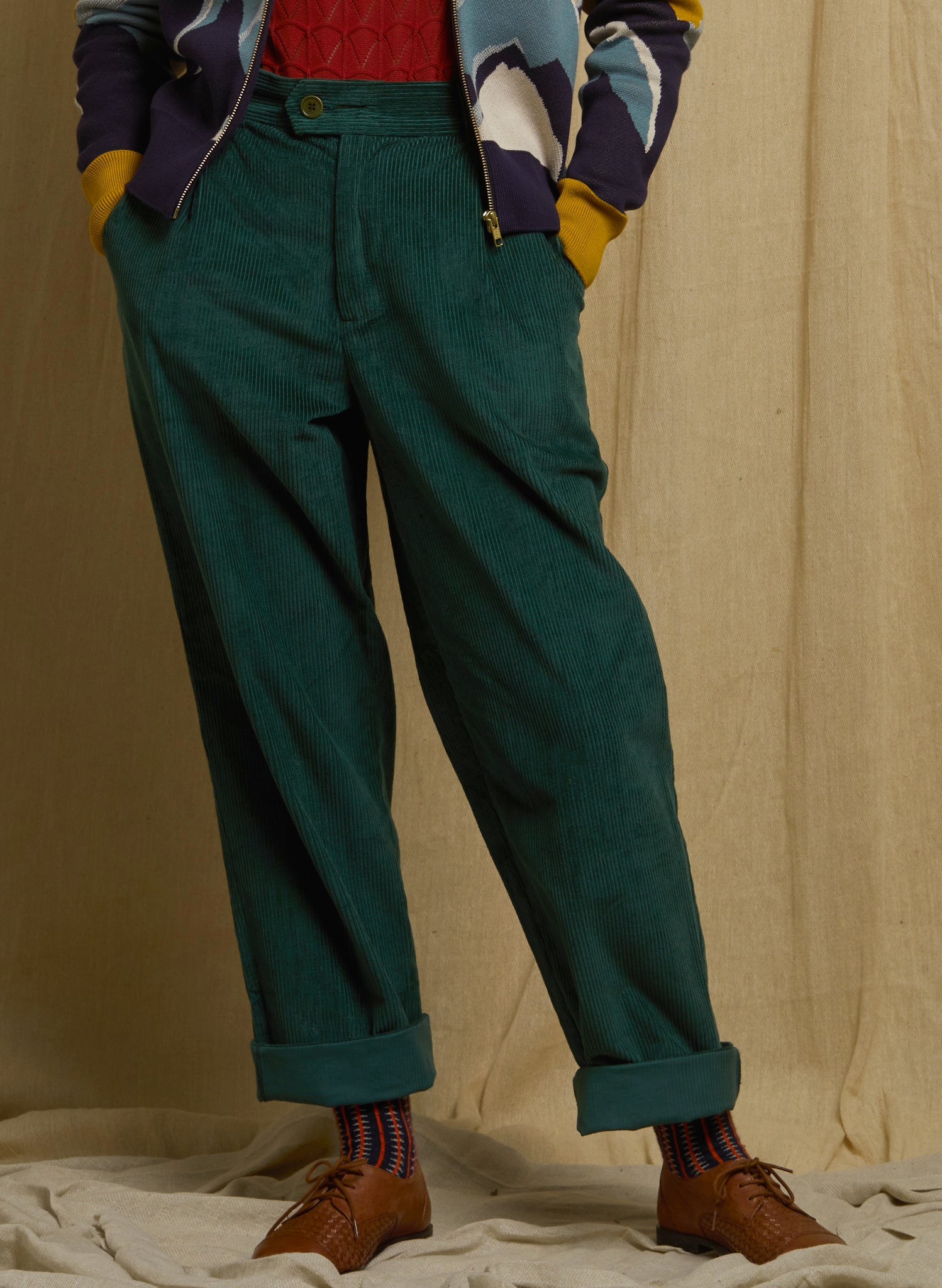 Person wearing green pants and a colorful jacket against a beige background