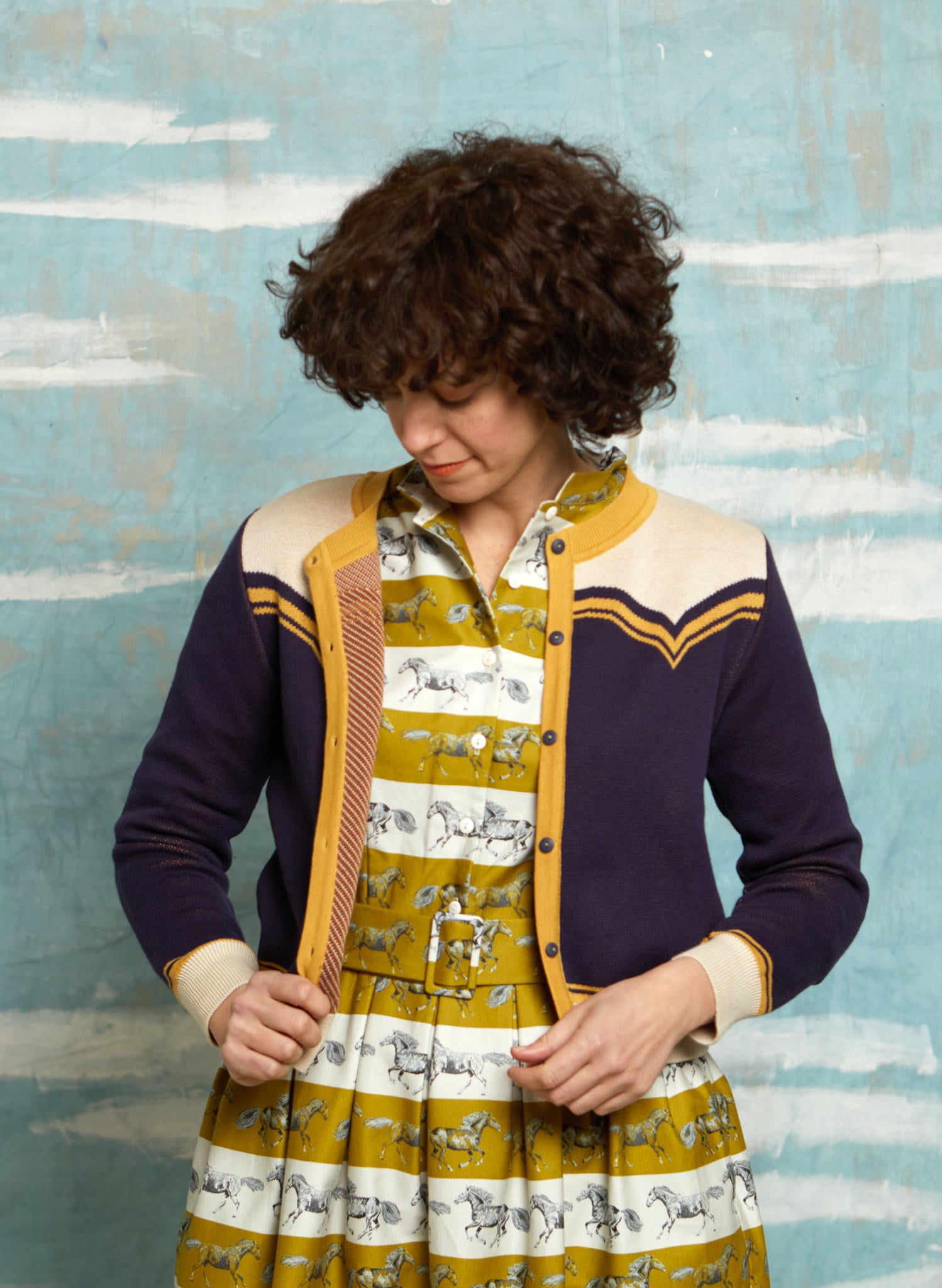 vintage style organic cotton knit cardigan in navy, white, and mustard with horse in the back