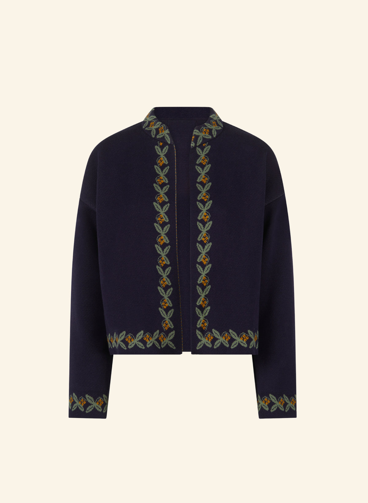 A cropped navy blue cardigan featuring vertical and horizontal floral embroidery in green, orange, and beige along the collar, front opening, and cuffs, displayed against a solid cream background.