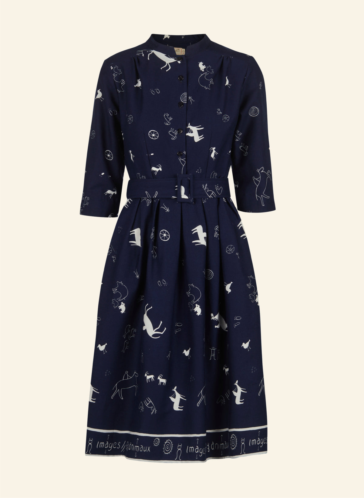 A navy blue midi dress with three-quarter sleeves, a button-up front, and a matching fabric tie belt at the waist. The dress features an all-over white whimsical print of cats, dogs, and birds, and a white printed border along the hem.