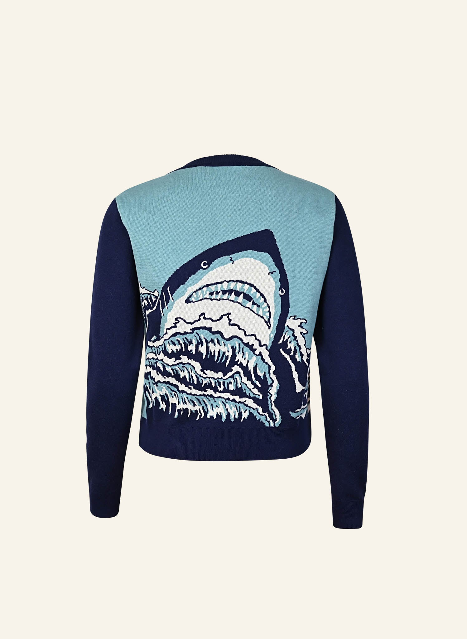 A flatshot image of the back of a teal and navy cardigan in a classic vintage style. The back features a graphic with a large sharks head looming over waves woven into the jacquard weave in teal navy and white.  