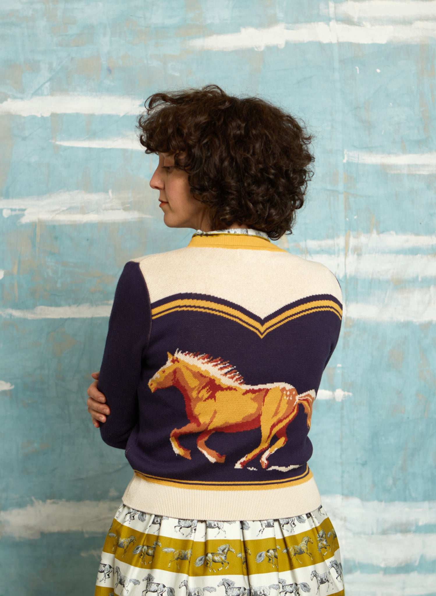 vintage style organic cotton knit cardigan in navy, white, and mustard with horse in the back