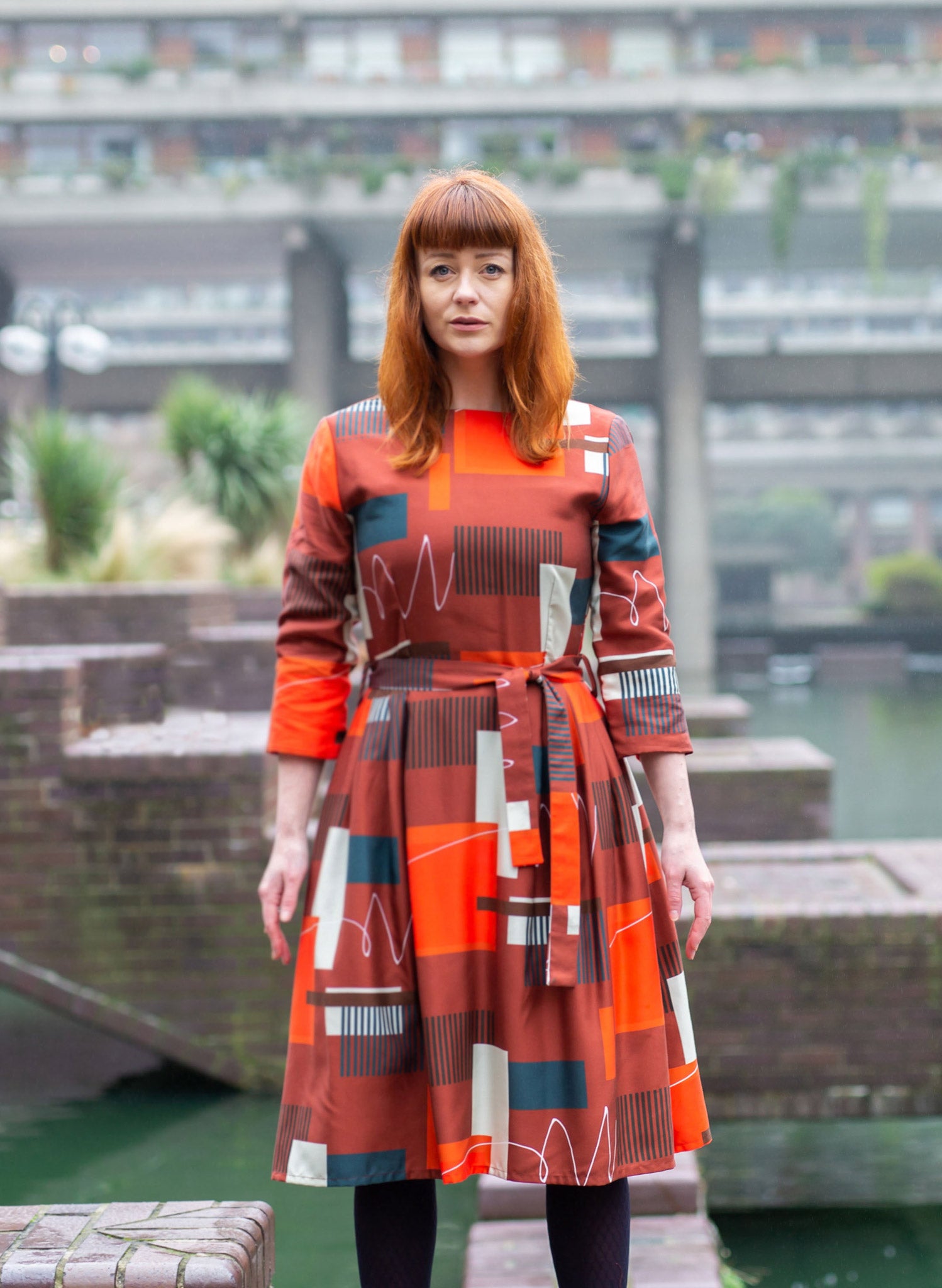 100% Tencel red, navy, and white knee-length dress with a tie-waist belt, 3/4 length sleeves, pockets, v-neck back, and abstract barbican print