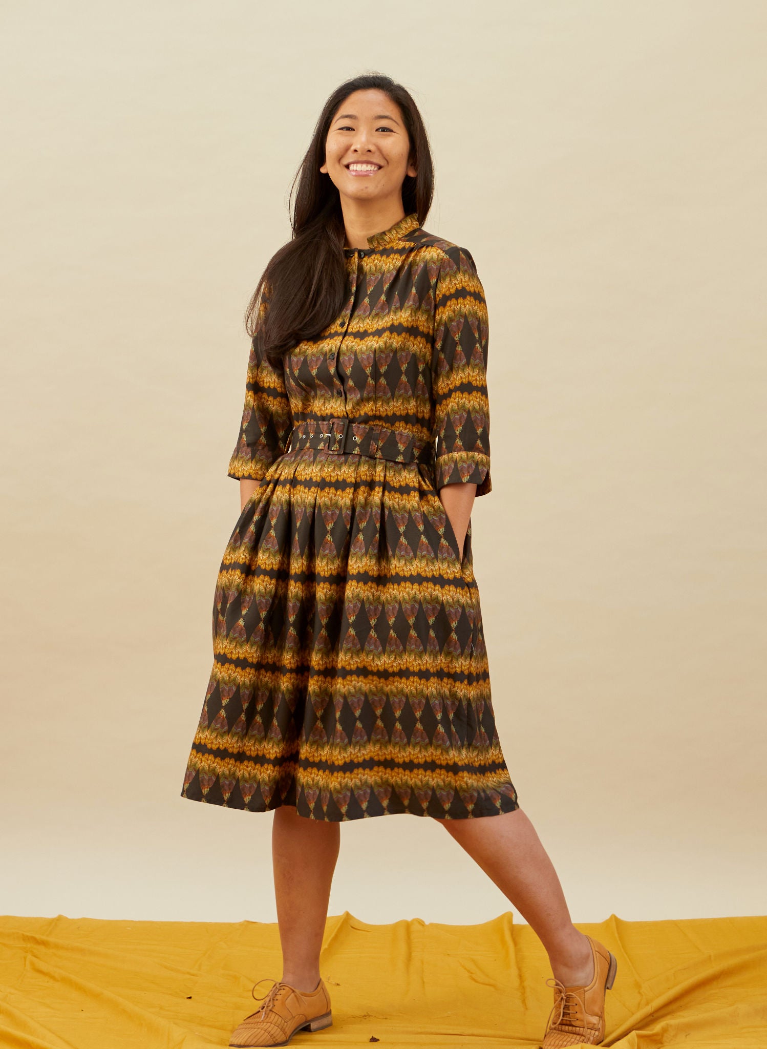 100% Tencel vintage-style gold and black knee-length belted shirt dress with 3/4 length sleeves, pockets, and a deco feather print