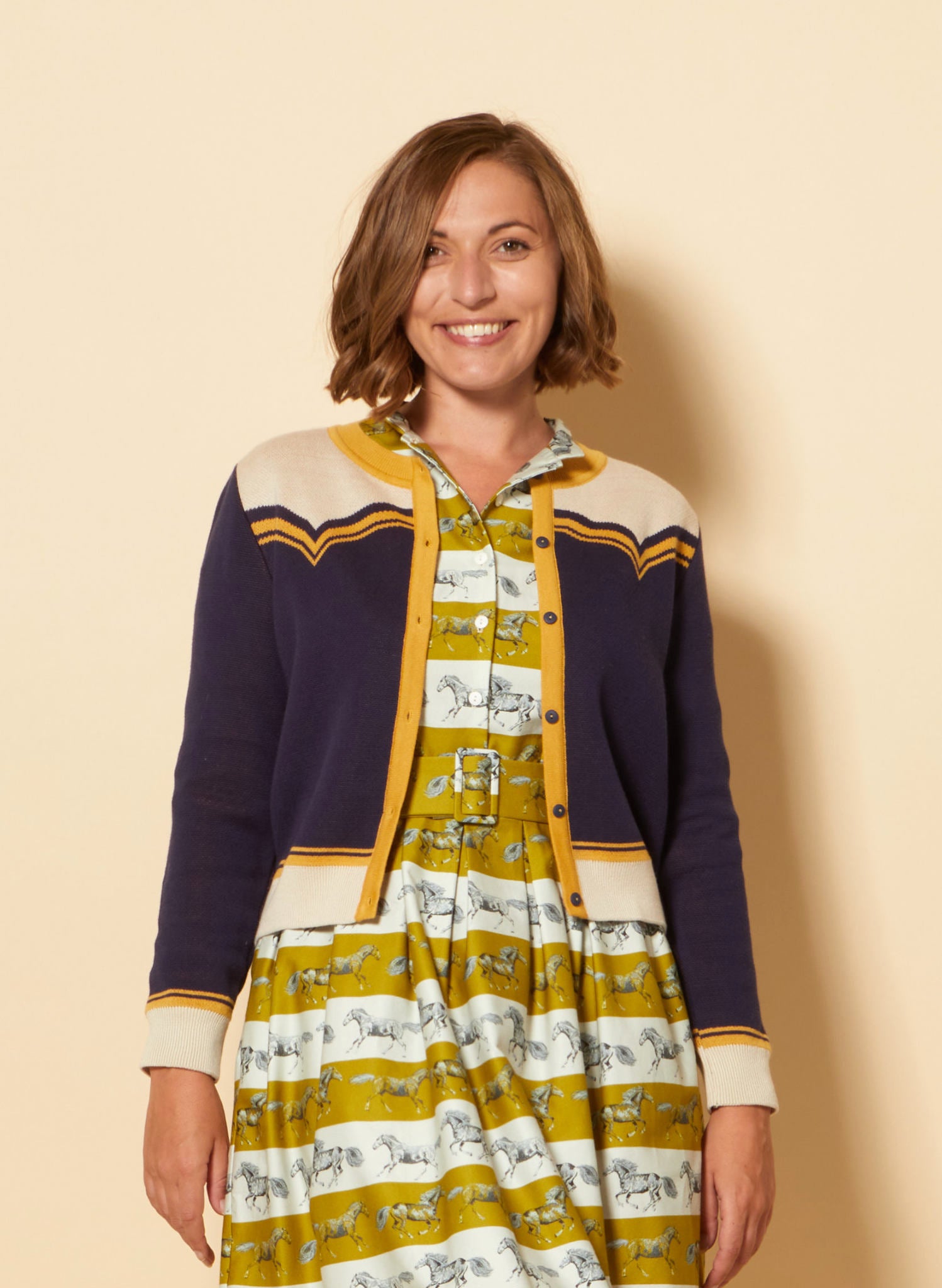 vintage style organic cotton knit cardigan in navy, white, and mustard with horse in the back
