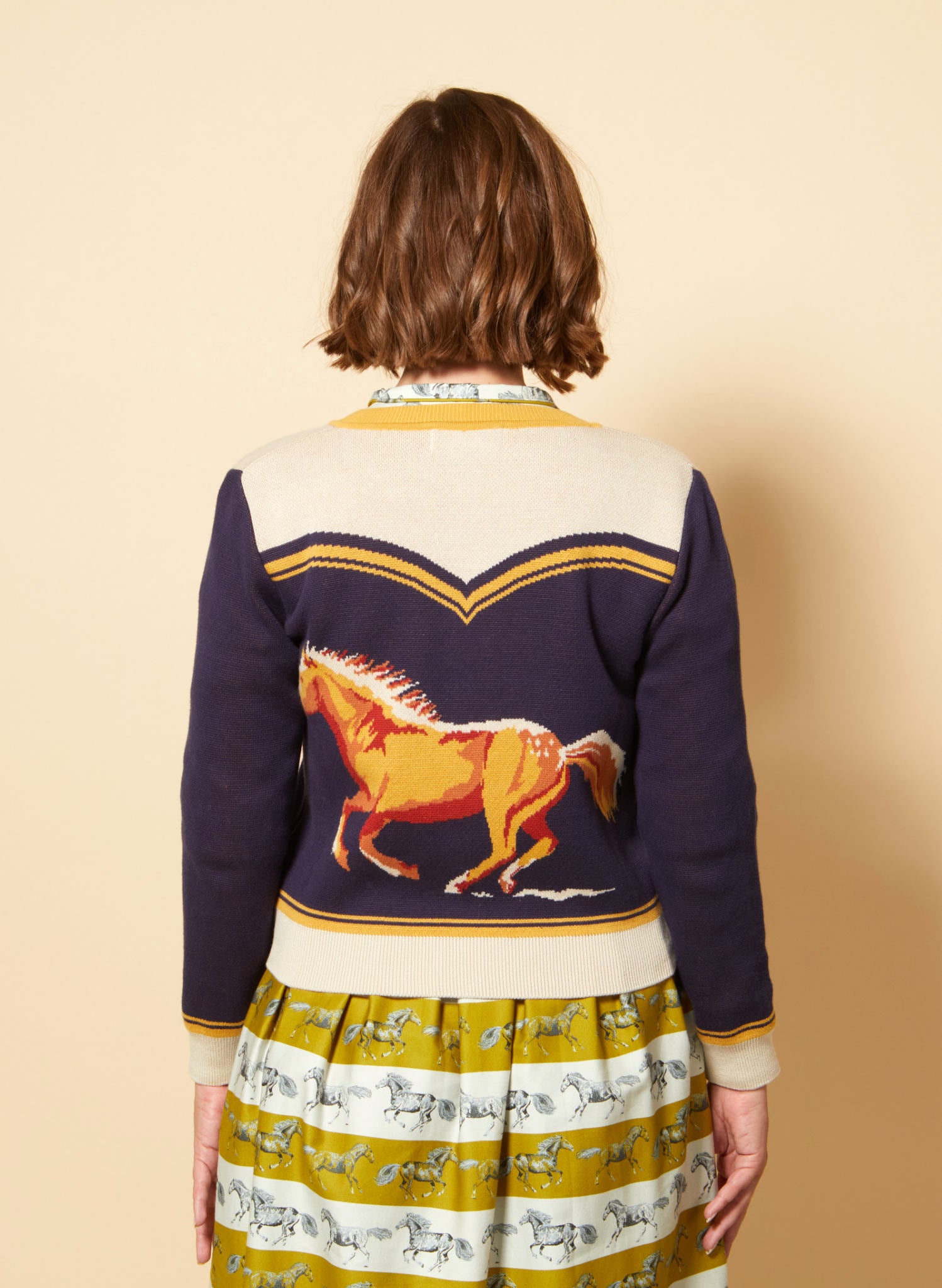 vintage style organic cotton knit cardigan in navy, white, and mustard with horse in the back